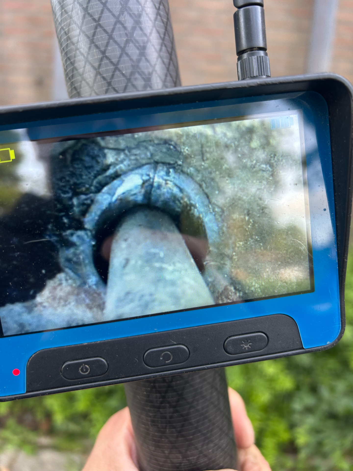 Inspectiescherm aan de telescoopstok toont een schone dakgoot met de afvoerpijp